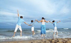 A family of four holding hands while they jump in the air at a beach